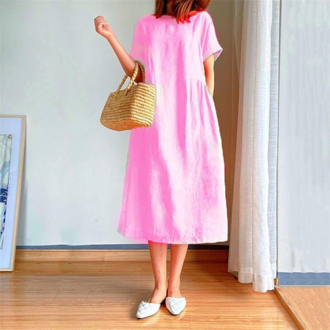 Women's Margot pink linen short sleeve midi dress with a straw bag and white flats.