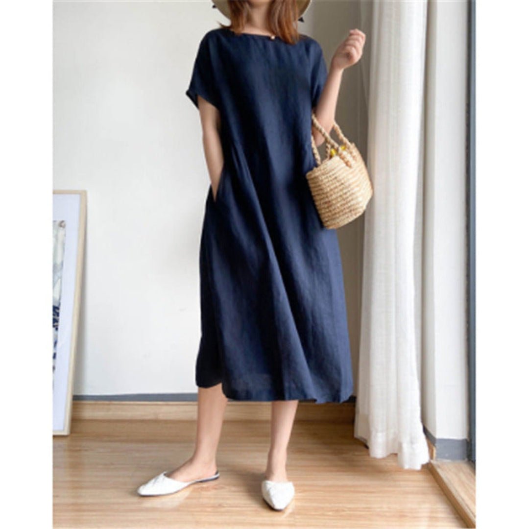 Women's navy linen short sleeve midi dress with pockets, paired with white flats and a straw bag.