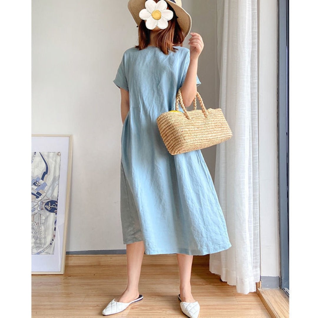Woman in a light blue linen short sleeve midi dress, straw hat, and woven bag.