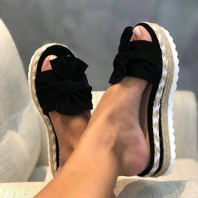 Black bow platform slide sandals with espadrille sole on feet.