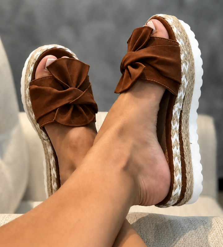 Women's brown bow platform slide sandals with espadrille-style woven soles and white outsoles.