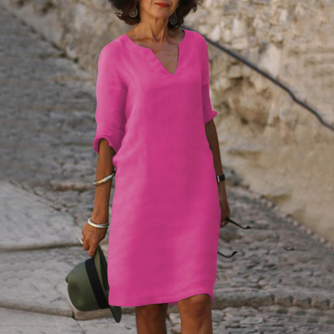 Woman wearing a vibrant fuchsia Mia summer dress with a flattering V-neck and 3/4 sleeves, holding a hat.