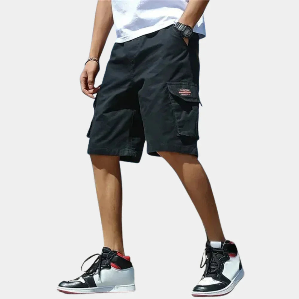 Men wearing black loose-fit cargo shorts with side pockets, drawstring waist, and casual streetwear style.