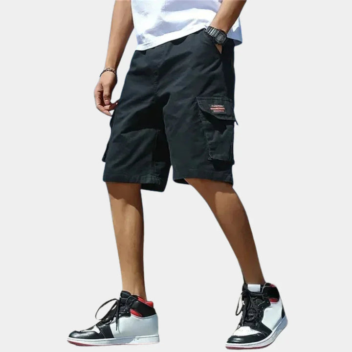 Men wearing black loose-fit cargo shorts with side pockets, drawstring waist, and casual streetwear style.