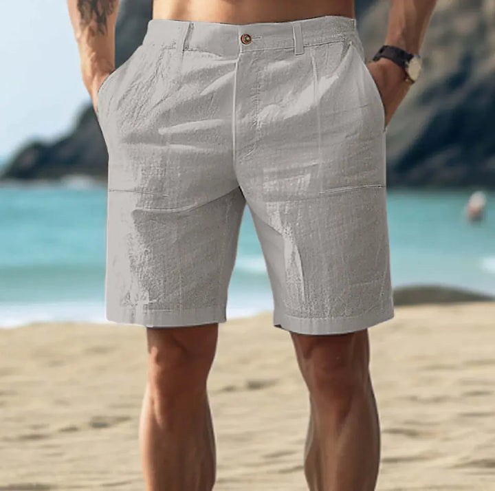 Men's light gray above-knee shorts with a button-front waist, belt loops, and front pockets, on a beach.