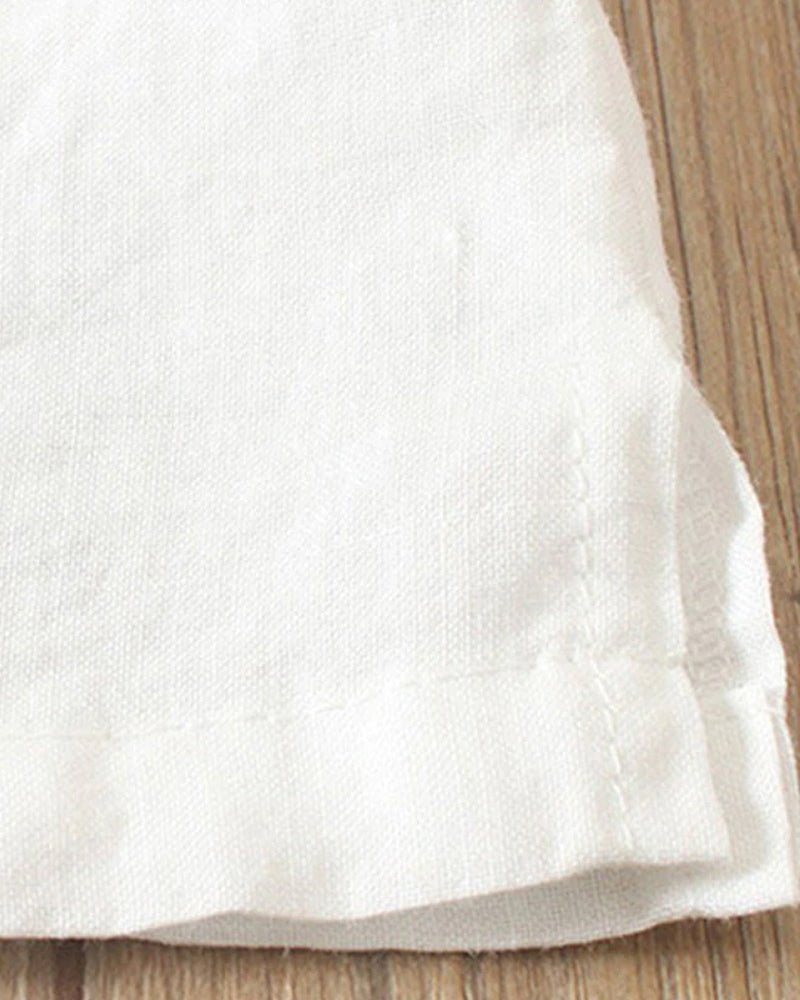 Close-up of white linen tunic fabric showing the hemline, side slit detail, and breathable woven texture.