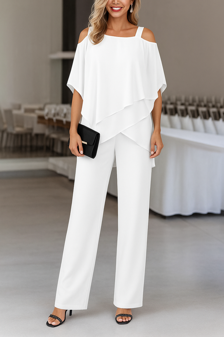 Woman in a white Odessa cold shoulder wide leg jumpsuit with a layered draped overlay, holding a black clutch.