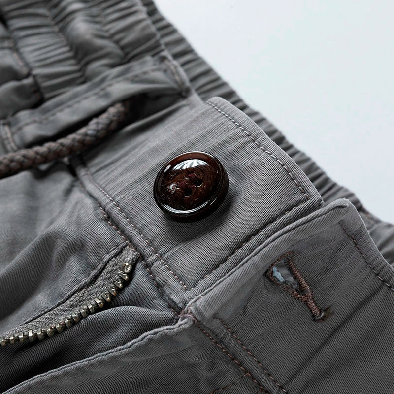 Close-up of men's gray drawstring cargo shorts with a dark brown button, zipper, and elastic waist.