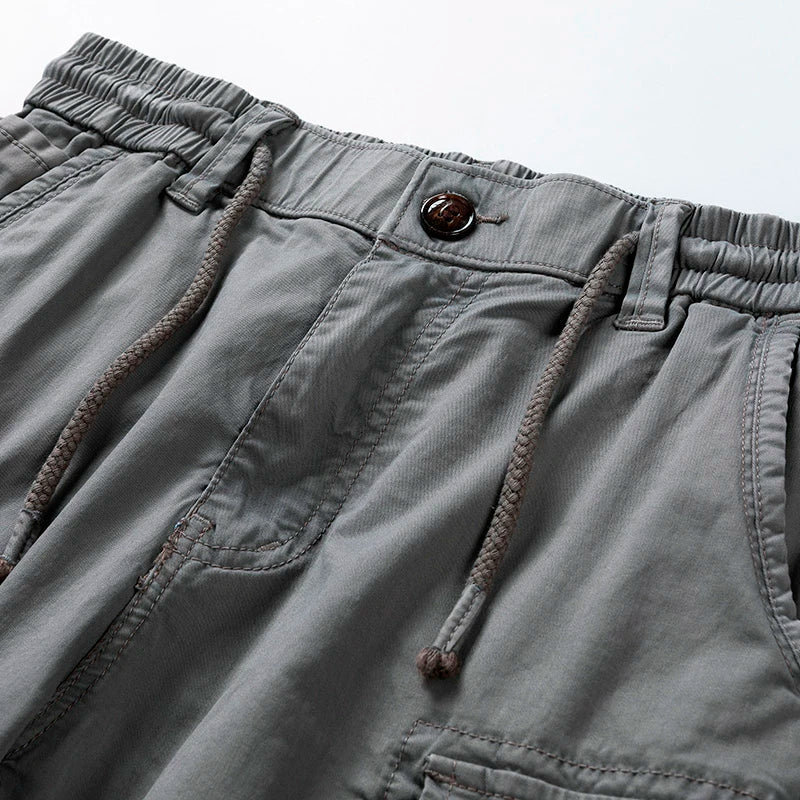 Close-up of gray men's drawstring cargo shorts with an elastic waist, button, and visible stitching.