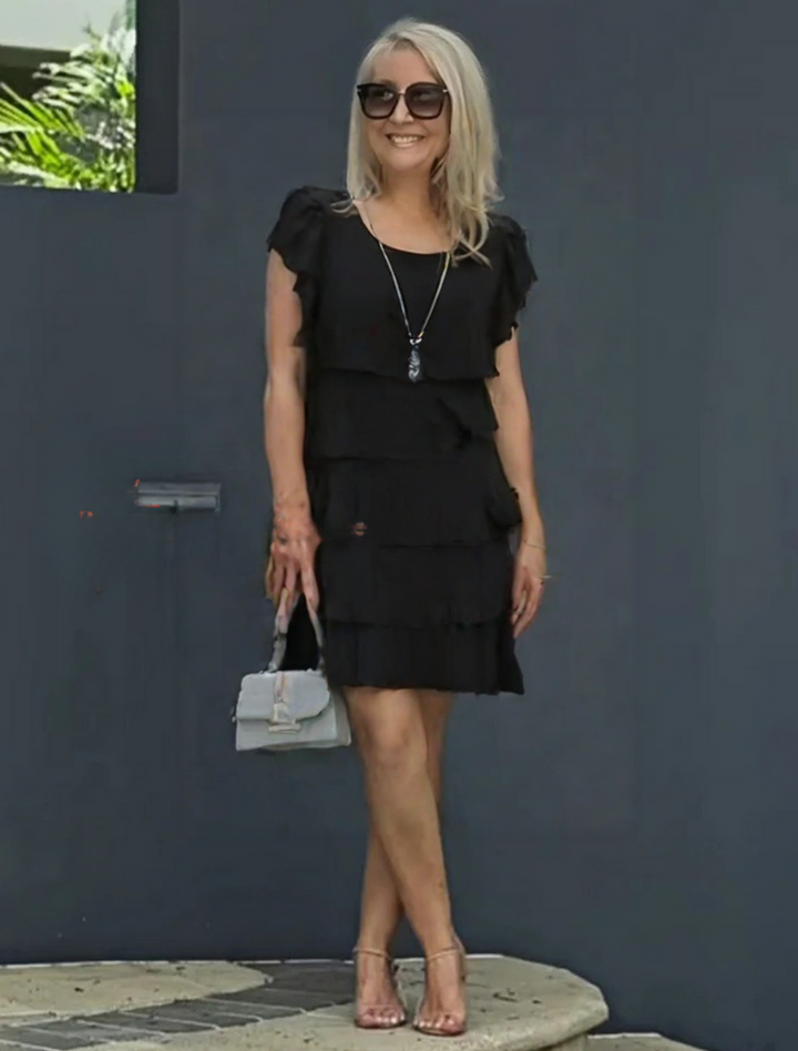 Sophia black short sleeve layered midi dress, worn by a smiling woman, with a grey handbag and heels.
