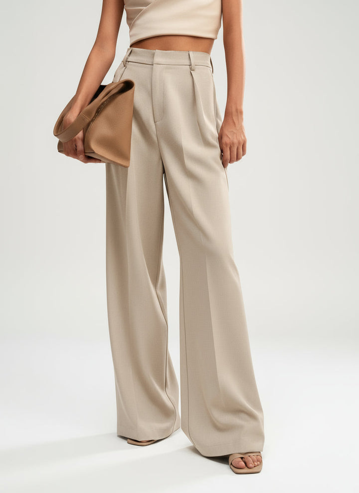 Stella women's high-waist, wide-leg beige pants with tailored lines, paired with a crop top and tan handbag.