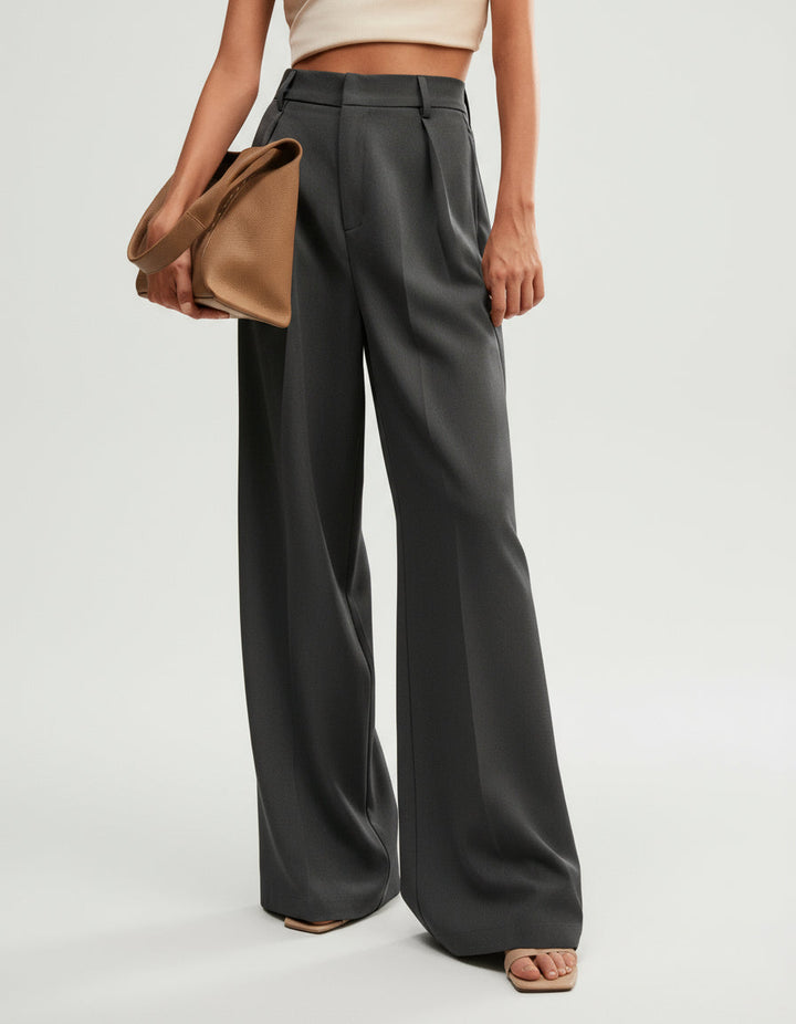 Stella women's charcoal high-waist wide-leg pants with tailored pleats, paired with a tan clutch and sandals.