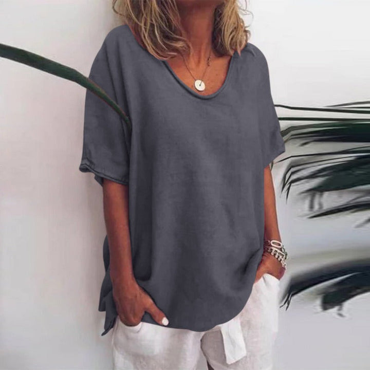 Charcoal grey V-neck flow blouse with short sleeves and a relaxed, draped fit worn with white trousers.
