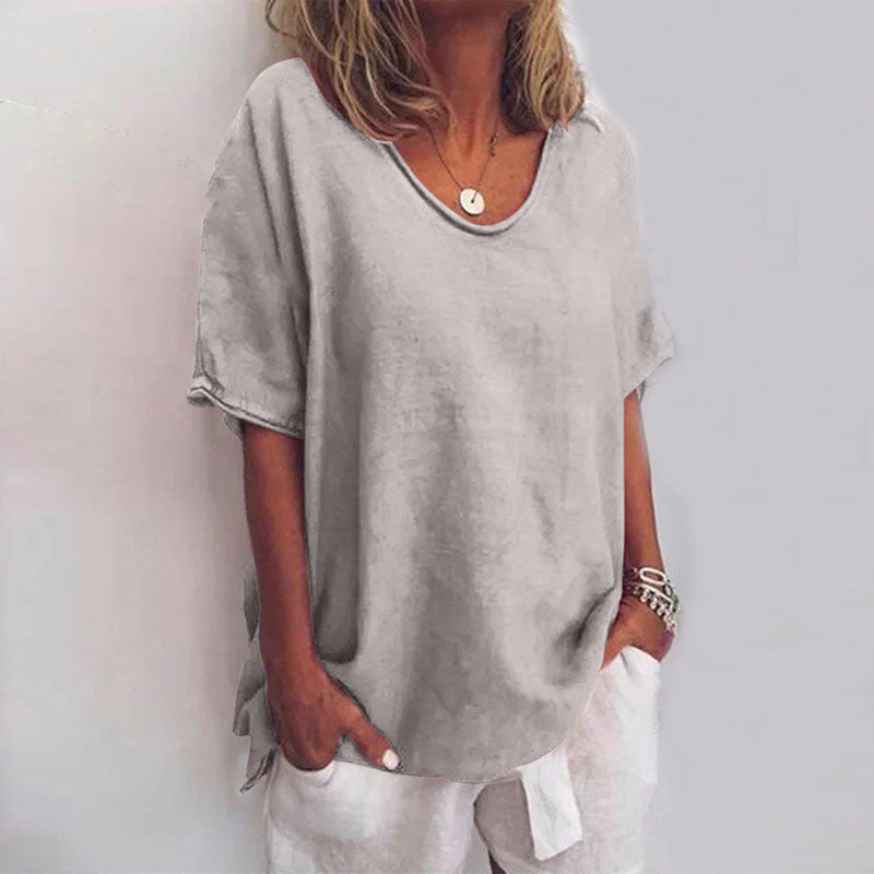 Soft grey V-neck flow blouse with short sleeves and a relaxed, draped fit worn with white trousers.