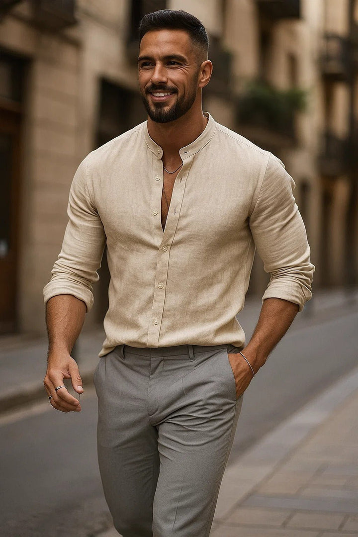 Smiling man in a beige linen band collar button-up shirt with rolled sleeves and grey pants.